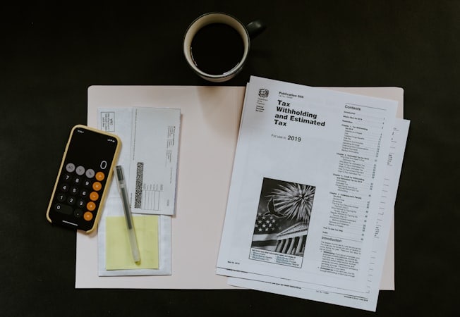 Tax documents, smartphone calculator, and coffee cup on a work desk