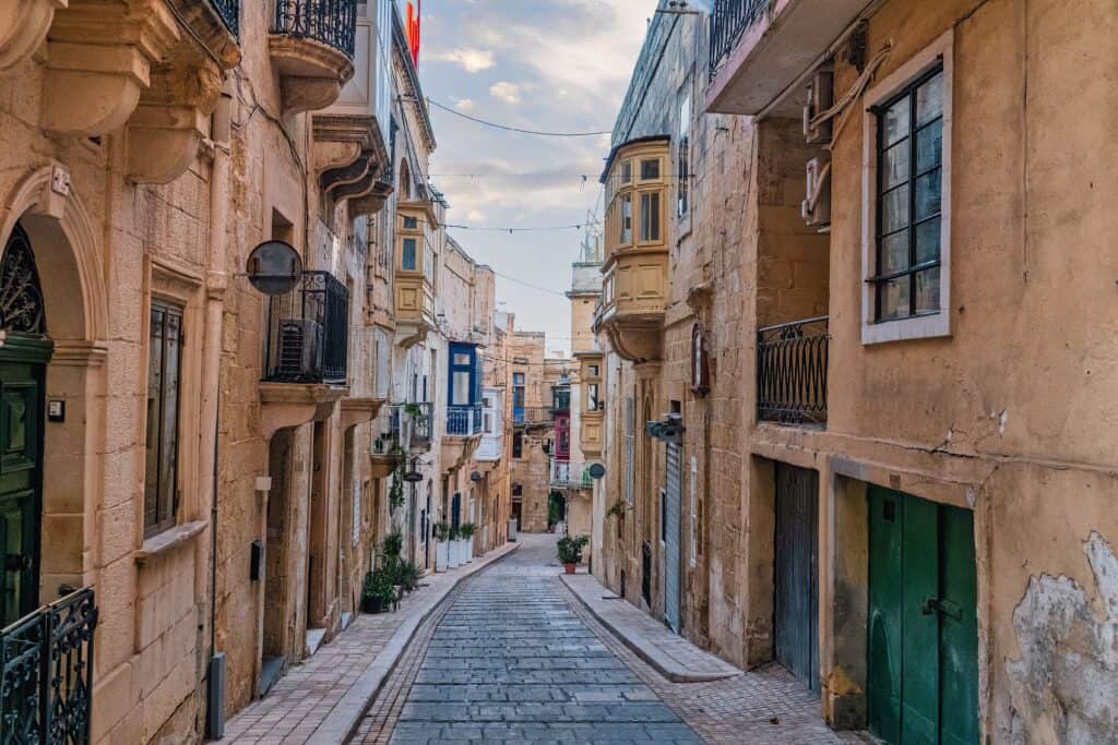 Narrow traditional street in Malta with limestone buildings and colourful balconies