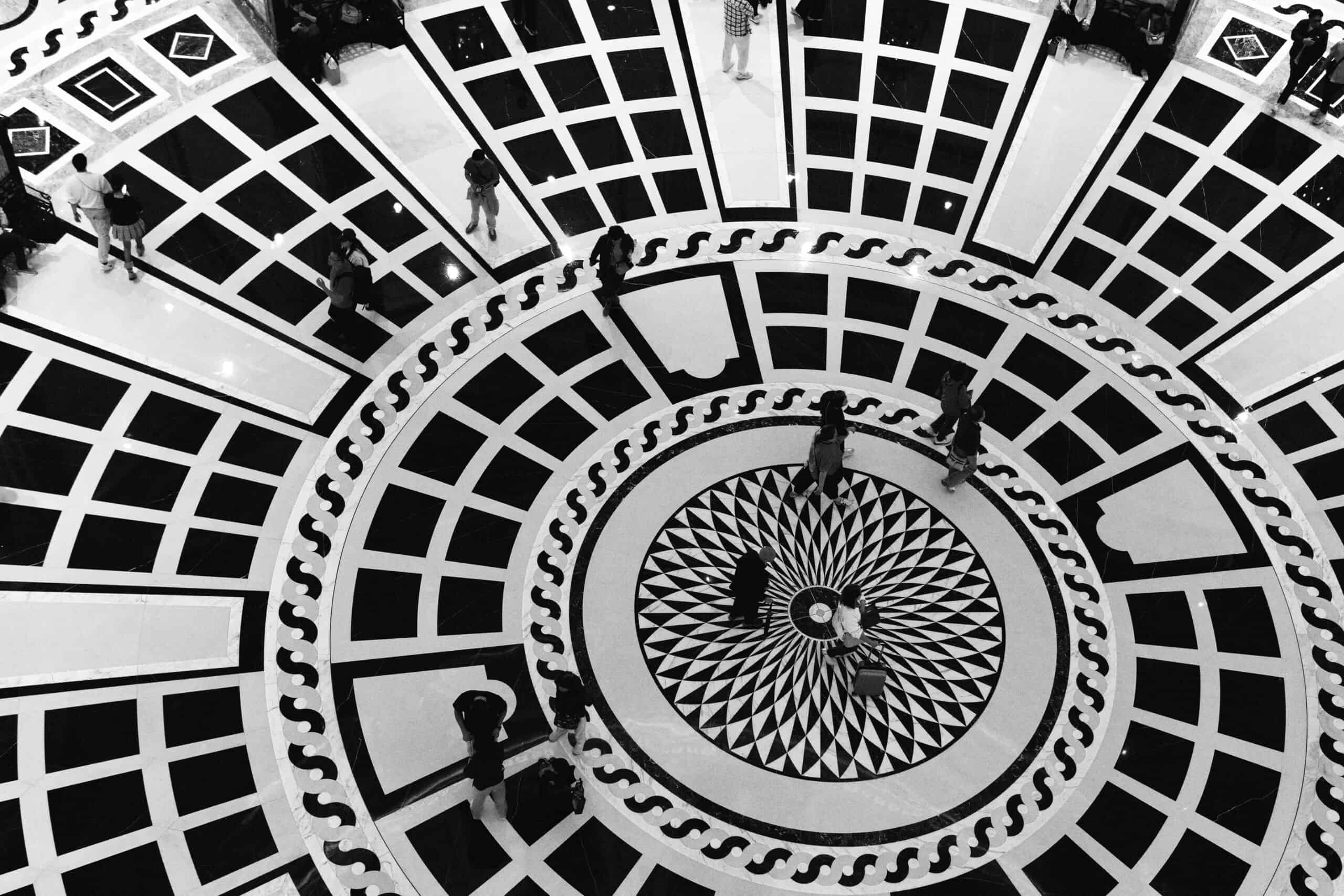 Looking down into a circular black-and-white atrium with people crossing the patterned floor