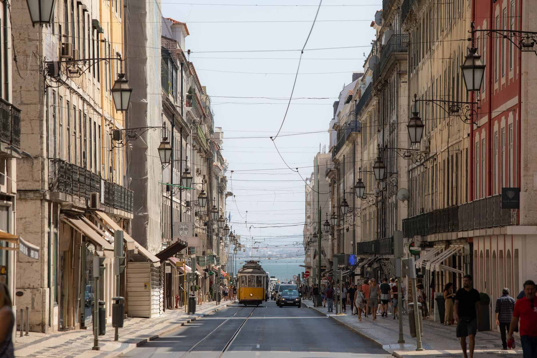 Classic Lisbon yellow tram passing historic buildings where international entrepreneurs settle and live